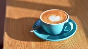 Een kop koffie met een hartmotief op een blauw schoteltje op een houten tafel.