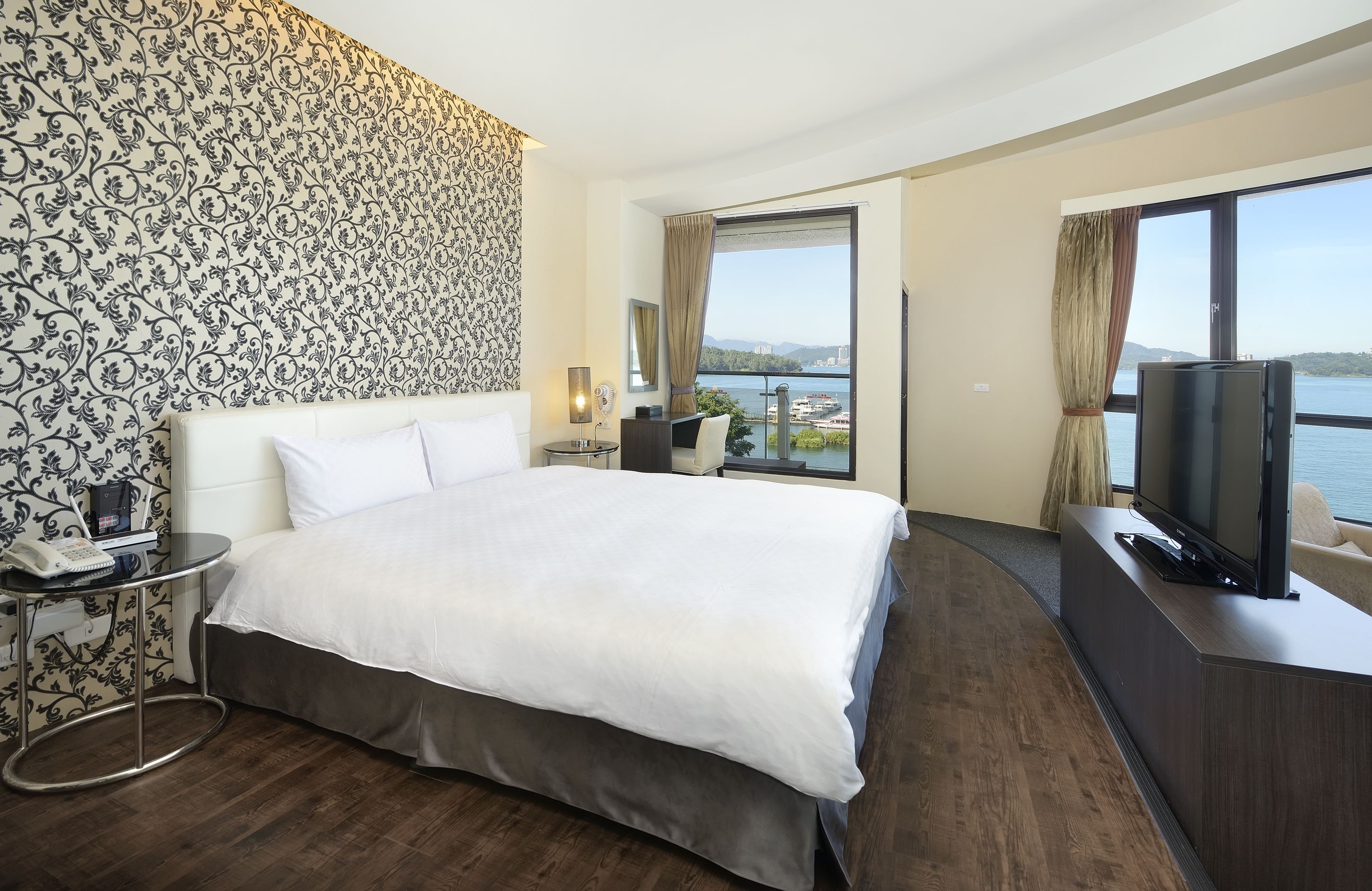 Habitación de hotel con una cama grande, televisión, escritorio y vista a un cuerpo de agua.