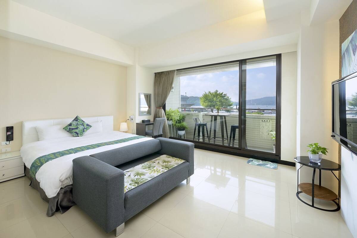 Una habitación de hotel moderna con una cama grande, un sofá, un televisor y un balcón con vistas a la ciudad.