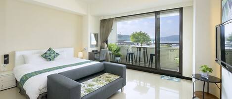 A modern hotel room with a large bed, a sofa, a TV, and a balcony with a view of the city.