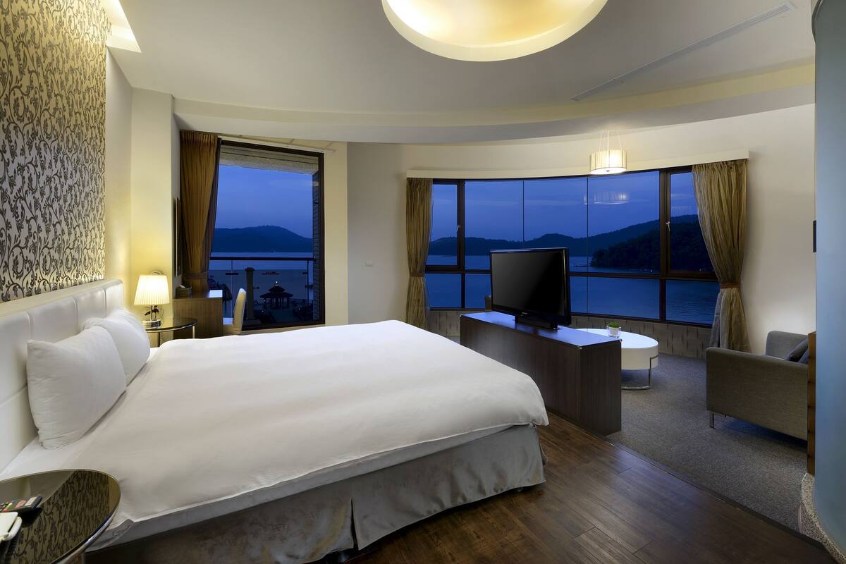 Habitación de hotel con una cama grande, un escritorio con televisor, un sofá y vista al mar.