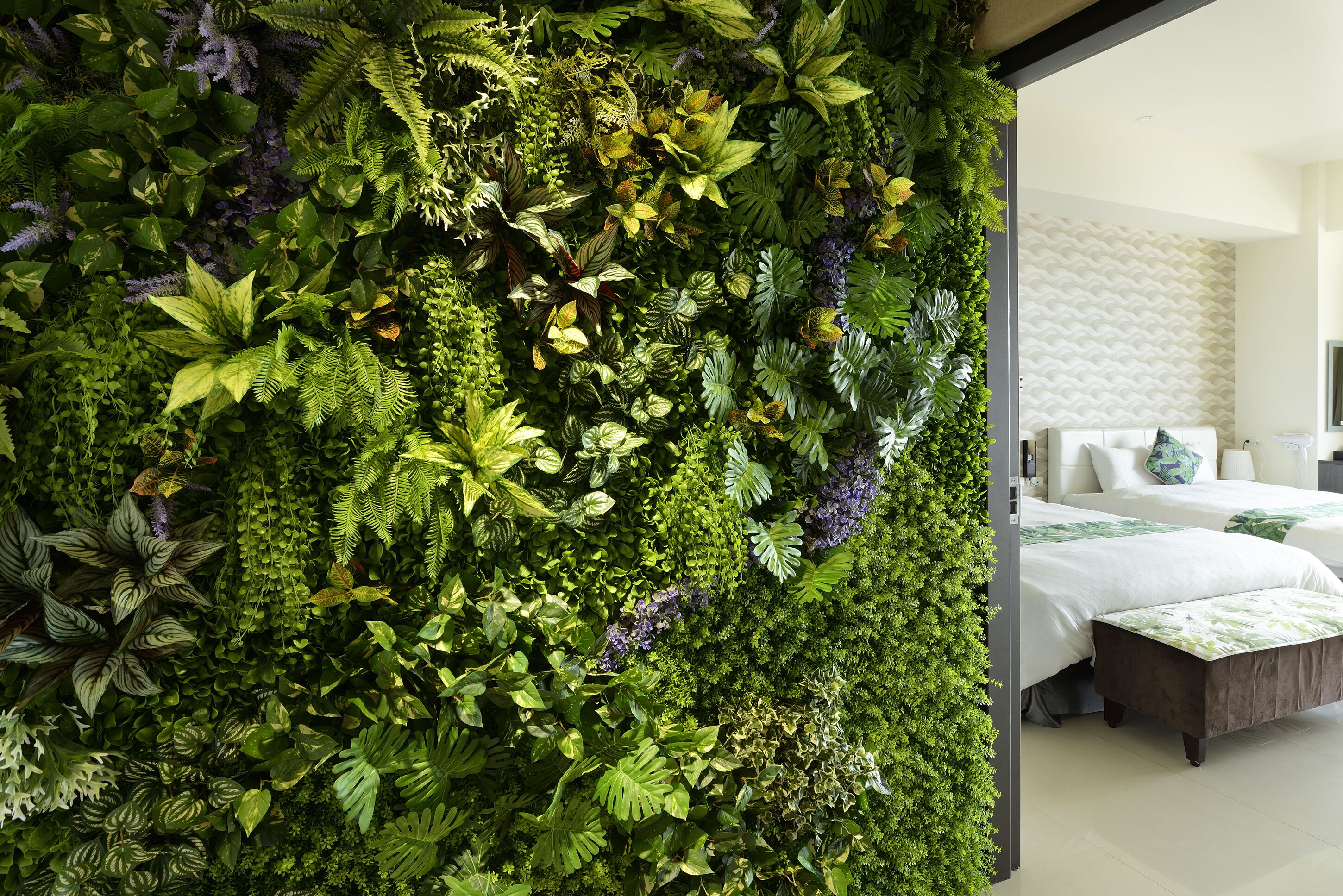Habitación con un jardín vertical verde, cama con ropa blanca y un baño moderno con un revestimiento de pared estampado.