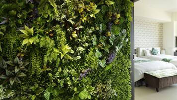 Habitación con un jardín vertical verde, cama con ropa blanca y un baño moderno con un revestimiento de pared estampado.