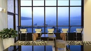 A room with a large window overlooking the sea, featuring a table and chairs, a potted plant, and patterned cushions. - Hu Yue Lakeview Hotel (Yuchi)