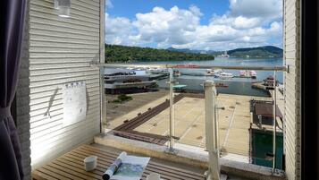 A balcony with a view of a marina, a wooden table with a cup and a magazine, and a window with blinds.