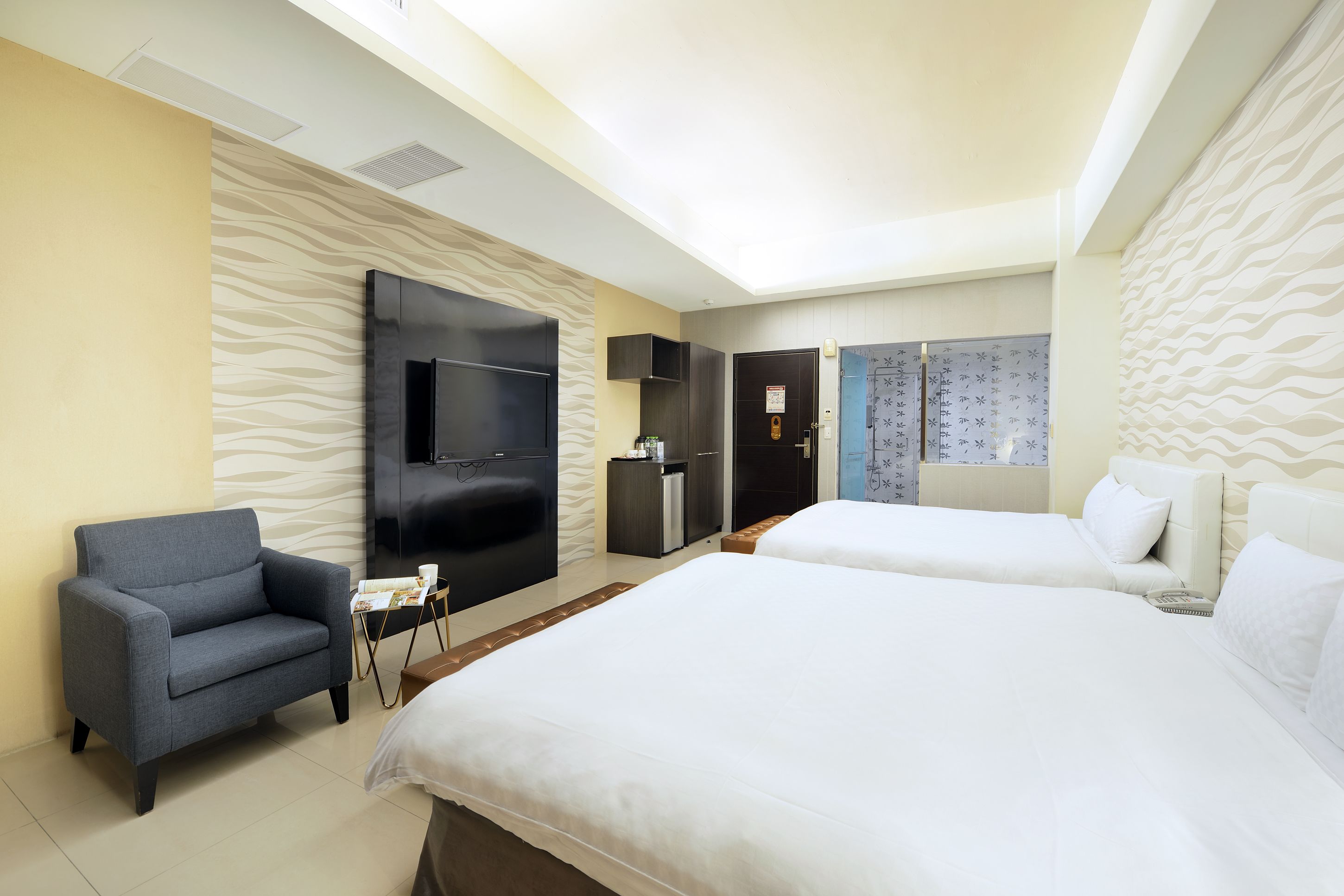 A hotel room with two beds, a flat-screen TV, a sofa, and a minibar.