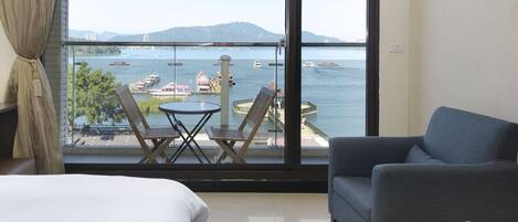 Habitación de hotel con un ventanal grande que ofrece vista a un cuerpo de agua, un balcón con asientos y una cama.