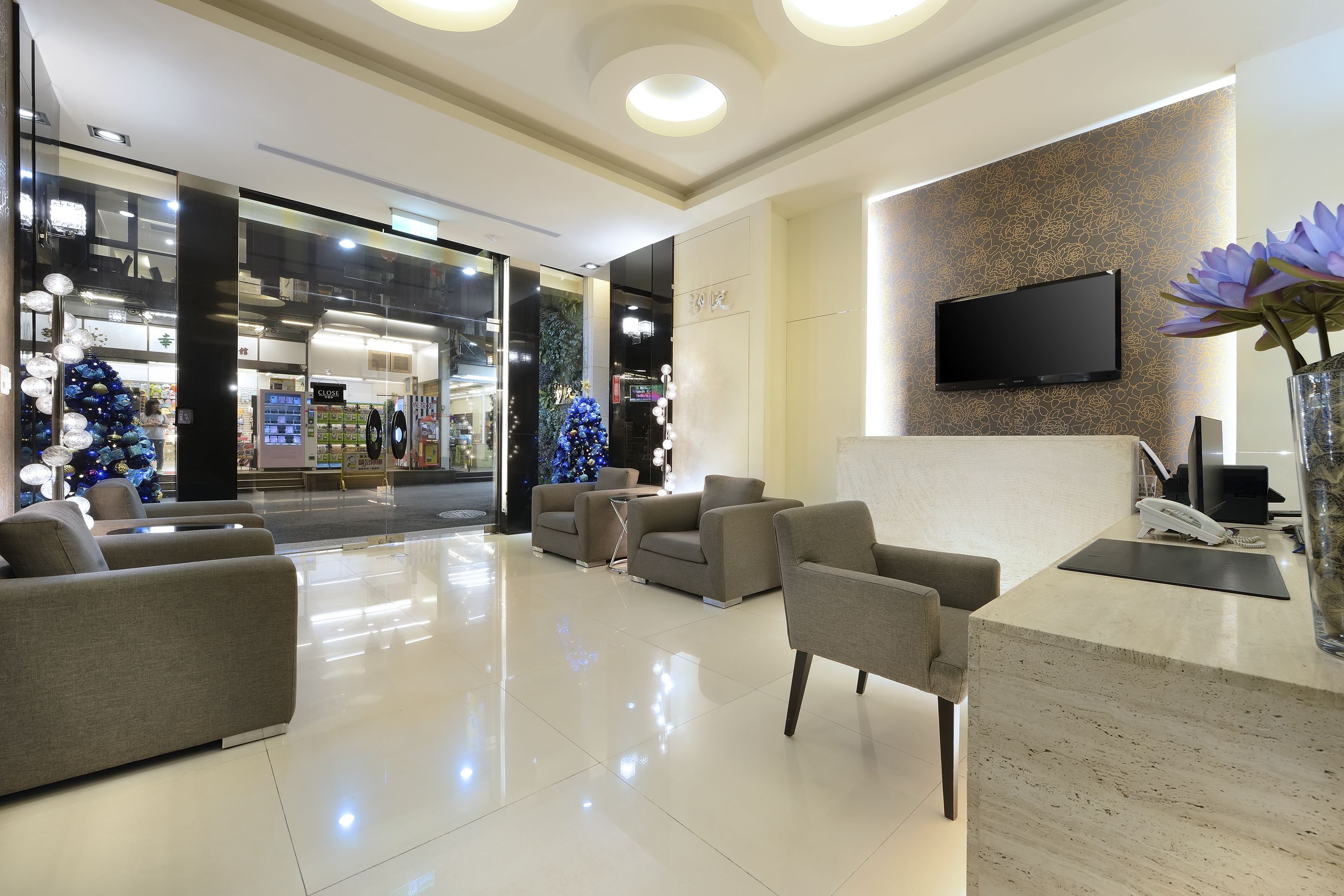 A modern lobby with a reception desk, seating area, and a large TV screen.