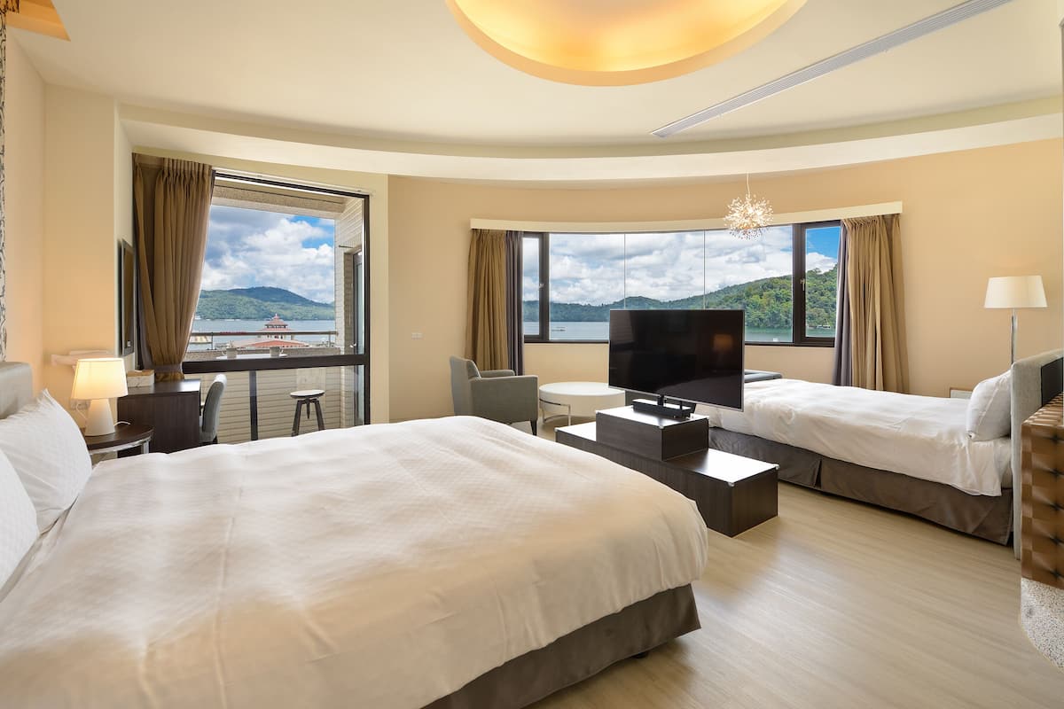Habitación de hotel con dos camas, televisión, escritorio y vistas a un lago y montañas.