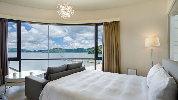 A hotel room with a large bed, a small table with two cups, a sofa, and a view of a lake and mountains. - Hu Yue Lakeview Hotel (Yuchi)