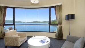 A room with a large bay window, a round white coffee table, a grey sofa, and a beige armchair. - Hu Yue Lakeview Hotel (Yuchi)