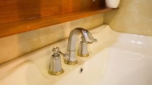 Une salle de bain avec une baignoire, deux robinets et une étagère en bois au-dessus du lavabo.