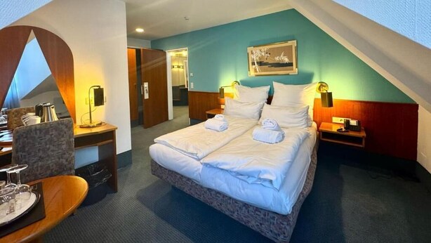 A hotel room with a bed, bedside tables, a desk, and a chair. - Lowen-seckenheim (Mannheim)