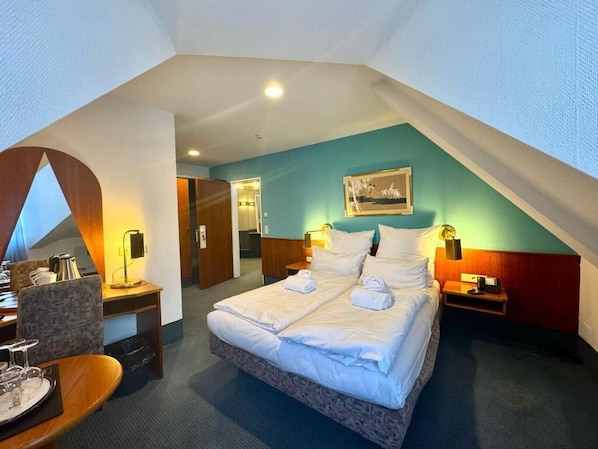 A hotel room with a bed, bedside tables, a desk, and a chair.