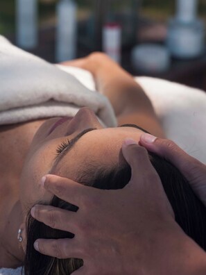 A person lying down with a hand on their head, suggesting a relaxing or spa-like setting.