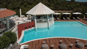 A pool with lounge chairs and umbrellas, a covered seating area, and a view of a forested hill. - Coluccia Hotel & Beach Club (Santa Teresa di Gallura)