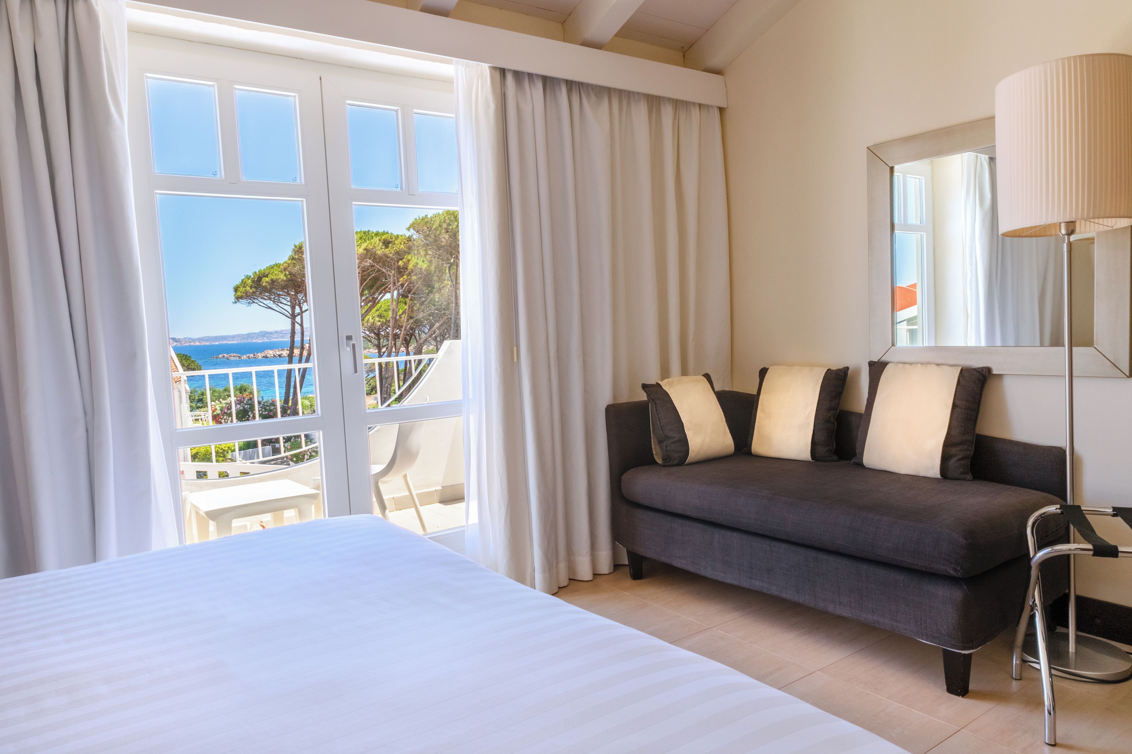 Une chambre d’hôtel comprenant un lit, un canapé, une chaise, une lampe et un balcon avec vue sur la mer.