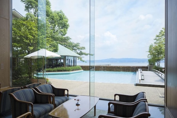 A room with a view of a swimming pool and a beach, furnished with chairs and a table.
