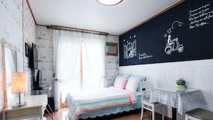 A bedroom with a bed, a desk, a chair, and a small table. There is a window with curtains, a wall with a chalkboard, and a wall with a scooter drawing. - Gangchon Sweet Pension (Chuncheon)