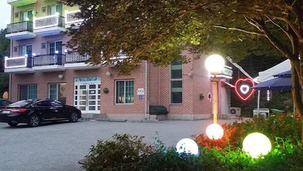 A building with a brick facade, a signboard, and a parked car. - Gangchon Sweet Pension (Chuncheon)