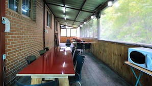 A covered dining area with brick walls, a long red table, and black chairs. - Gangchon Sweet Pension (Chuncheon)