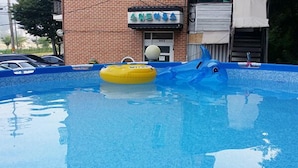 A swimming pool with inflatable toys and a brick building in the background. - Gangchon Sweet Pension (Chuncheon)