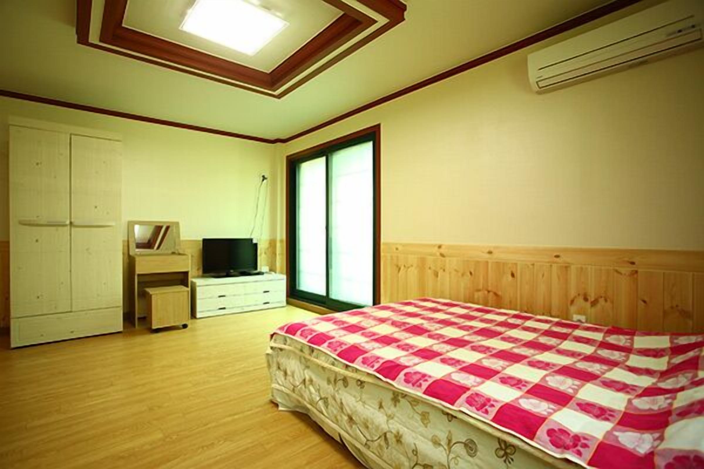 A bedroom with a bed, a TV, a wardrobe, and a window.