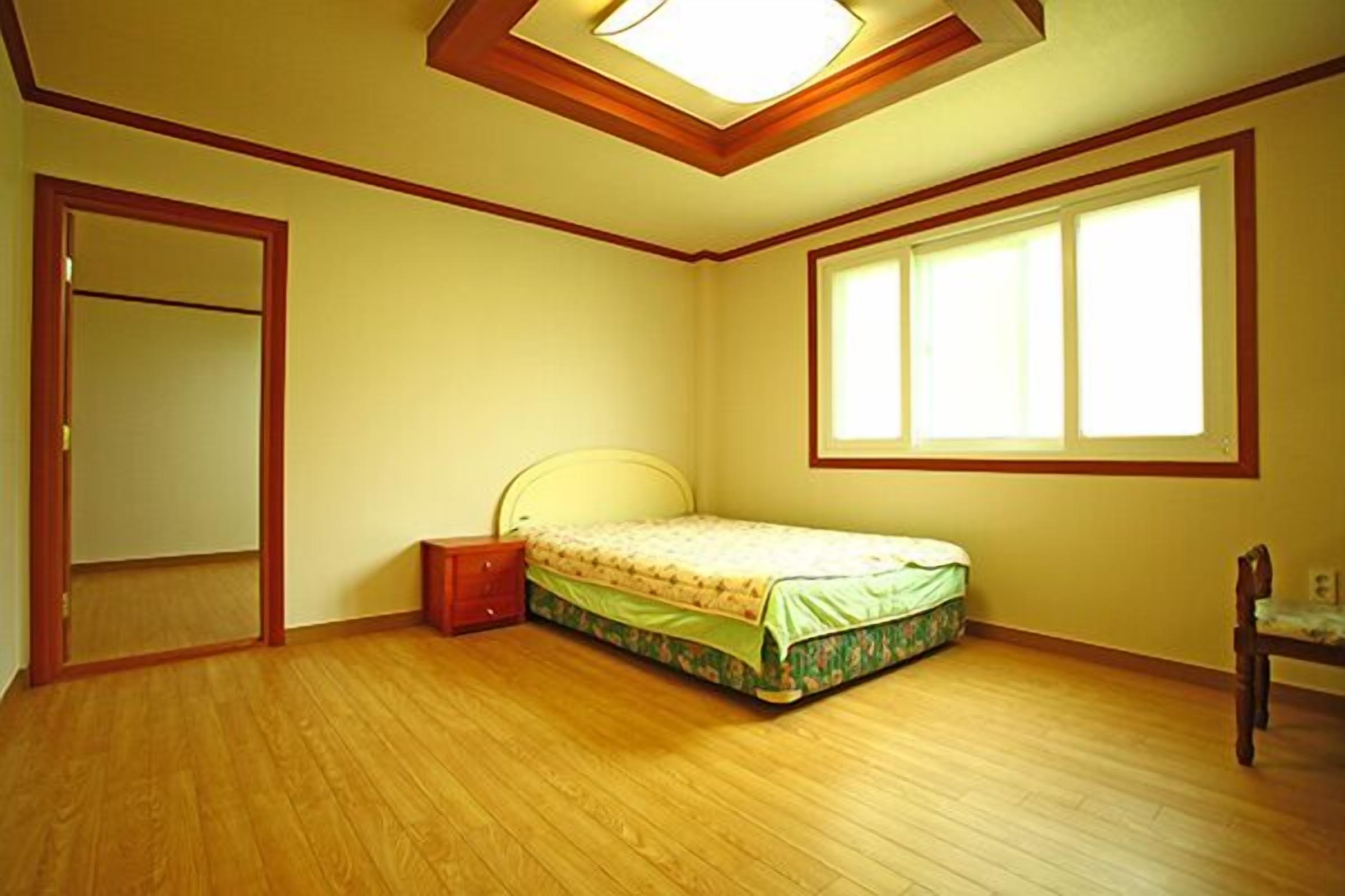Quarto com cama, mesa de cabeceira, cadeira, janela e porta.