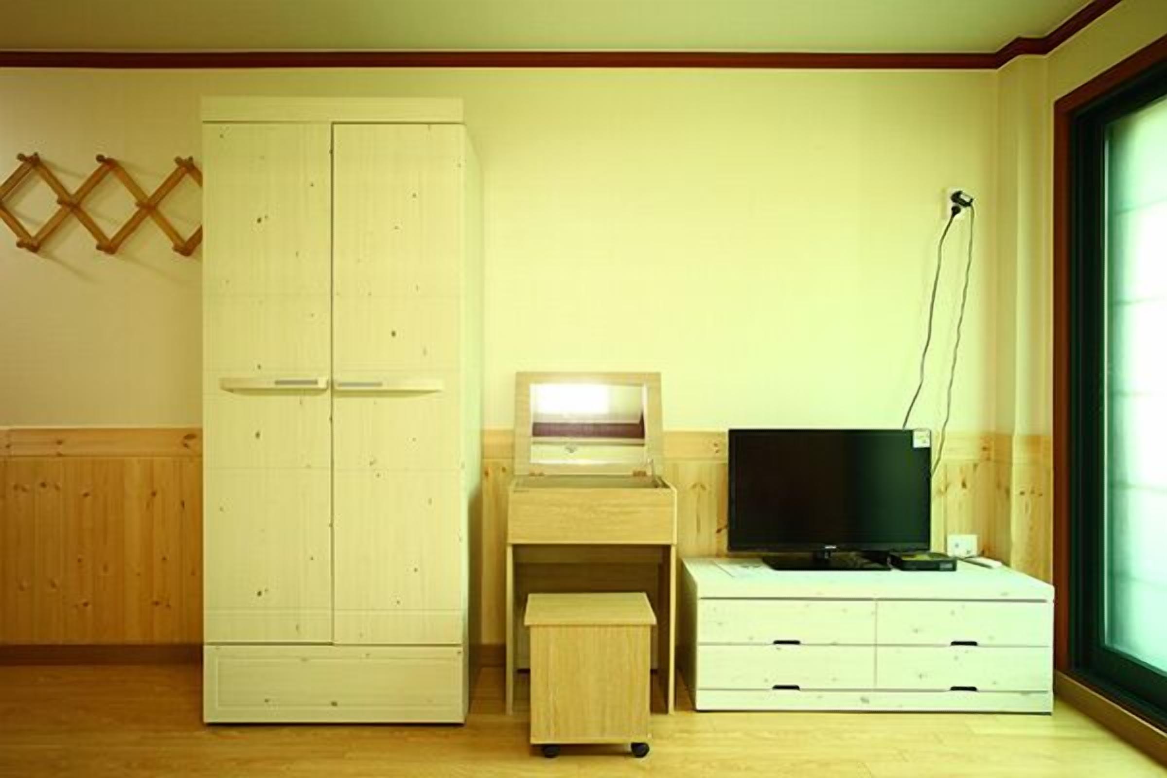 Ein Zimmer mit einem Holfischschrank, einem Schreibtisch mit Computer und einem Fernseher.