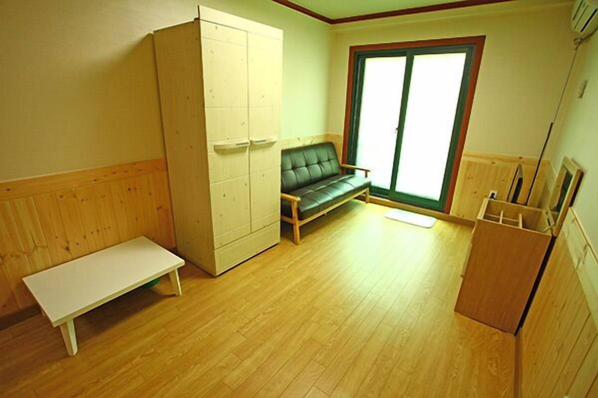 A room with a wooden floor, a green sofa, a white bench, a wardrobe, and a sliding glass door.