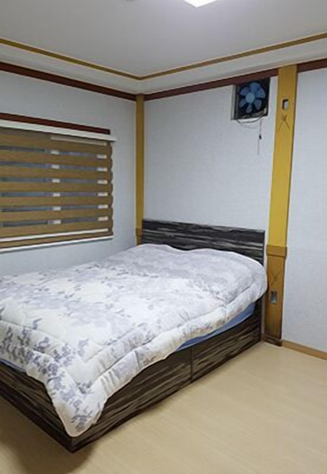 Un dormitorio con cama, ventana con persianas, aire acondicionado de pared y cabecero de madera.
