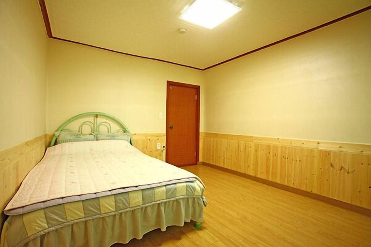 A bedroom with a bed, wooden floor, a door, and a light fixture.