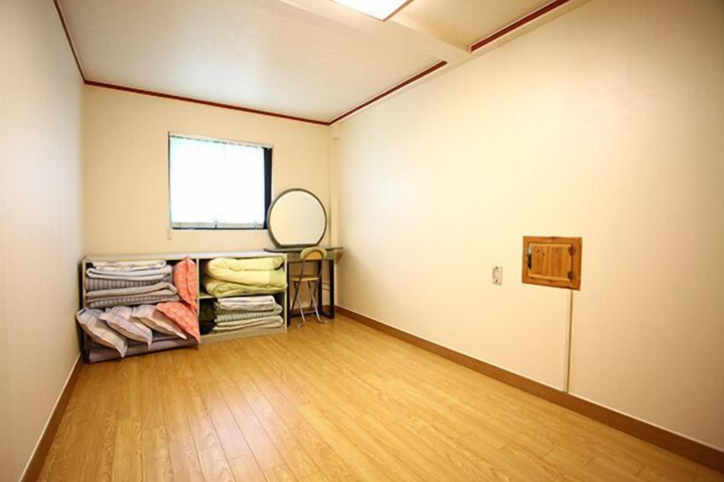 A room with wooden flooring, a window, a mirror, and a radiator.