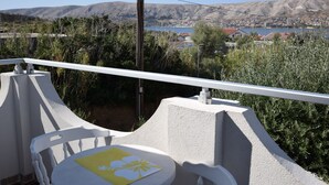 A balcony with a white railing, a table with a yellow placemat, and a view of a town and mountains in the background. - Comfortable apartment with balcony (Pag)