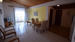 A dining area with a wooden table and chairs, a television, and a yellow wall with a painting. - Comfortable apartment with balcony (Pag)