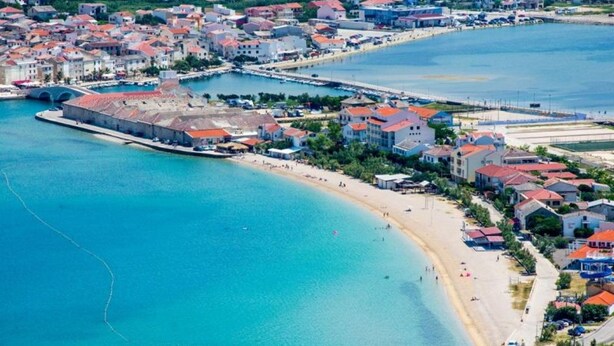 An aerial view of a coastal town with a beach, buildings, and a fortified structure. - Comfortable apartment with balcony (Pag)