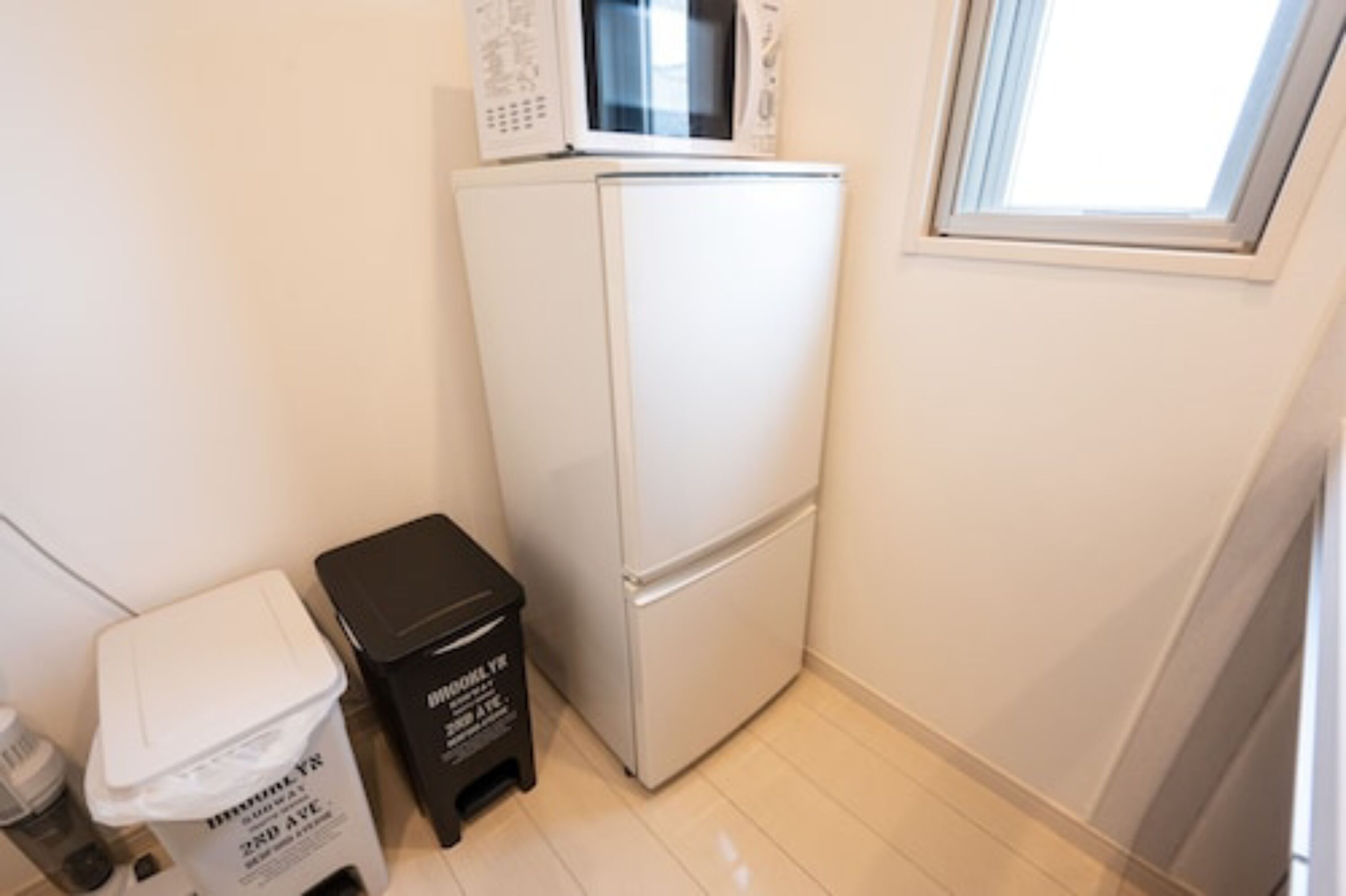 Una cocina compacta con un refrigerador blanco, un microondas y un basurero pequeño.