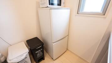 Una cocina compacta con un refrigerador blanco, un microondas y un basurero pequeño.