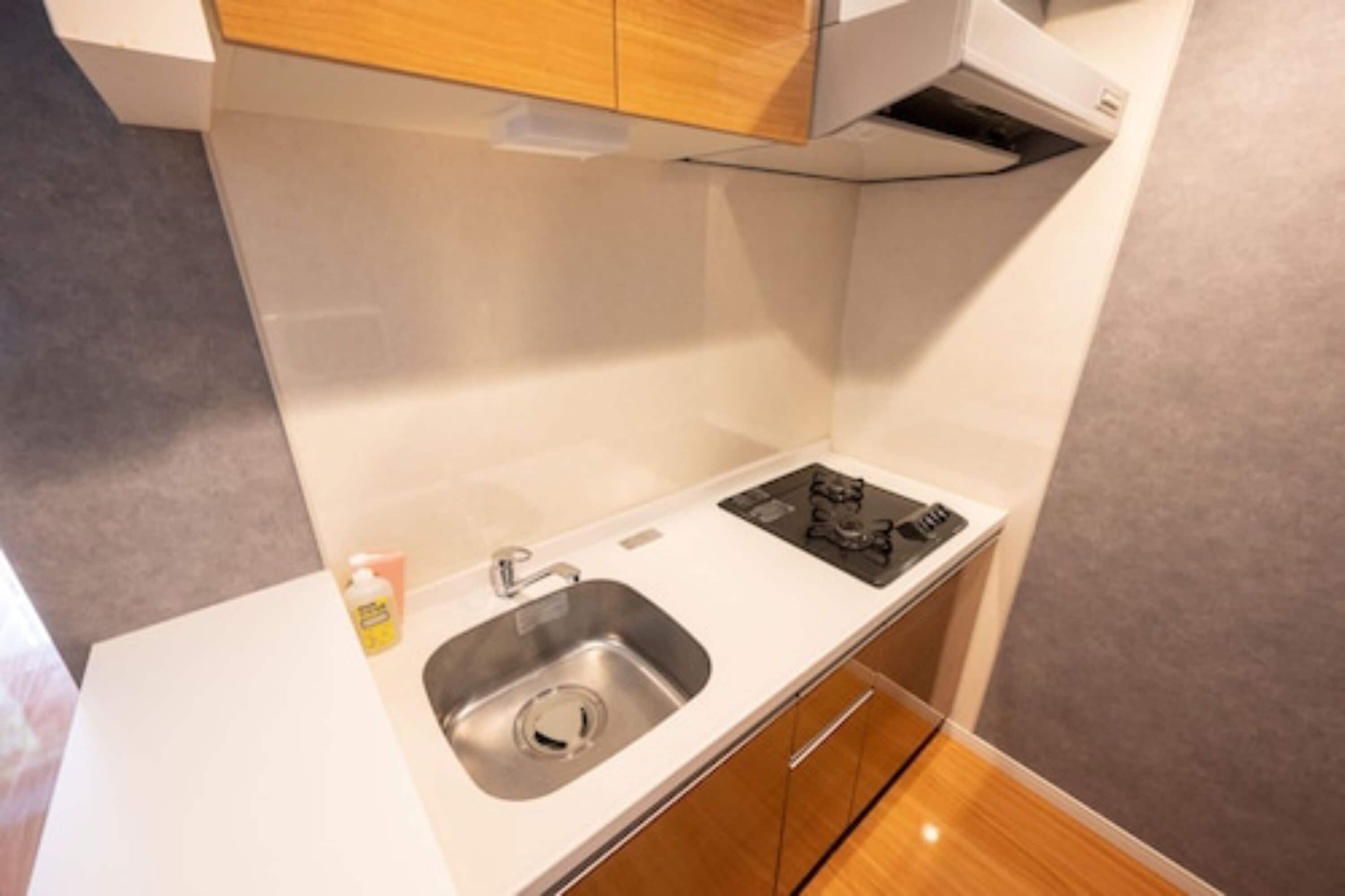 Une cuisine compacte dotée d’un évier en acier inoxydable, d’un petit plan de travail et d’armoires en bois.