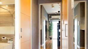 A modern hotel corridor with wooden flooring, a visible bathroom with a bathtub, and a potted plant in the distance. - Residence Hotel Hakata 8 (Fukuoka)
