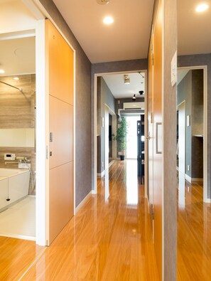 Un couloir d’hôtel moderne, avec un plancher en bois, une salle de bain visible avec une baignoire, et une plante en pot au loin.