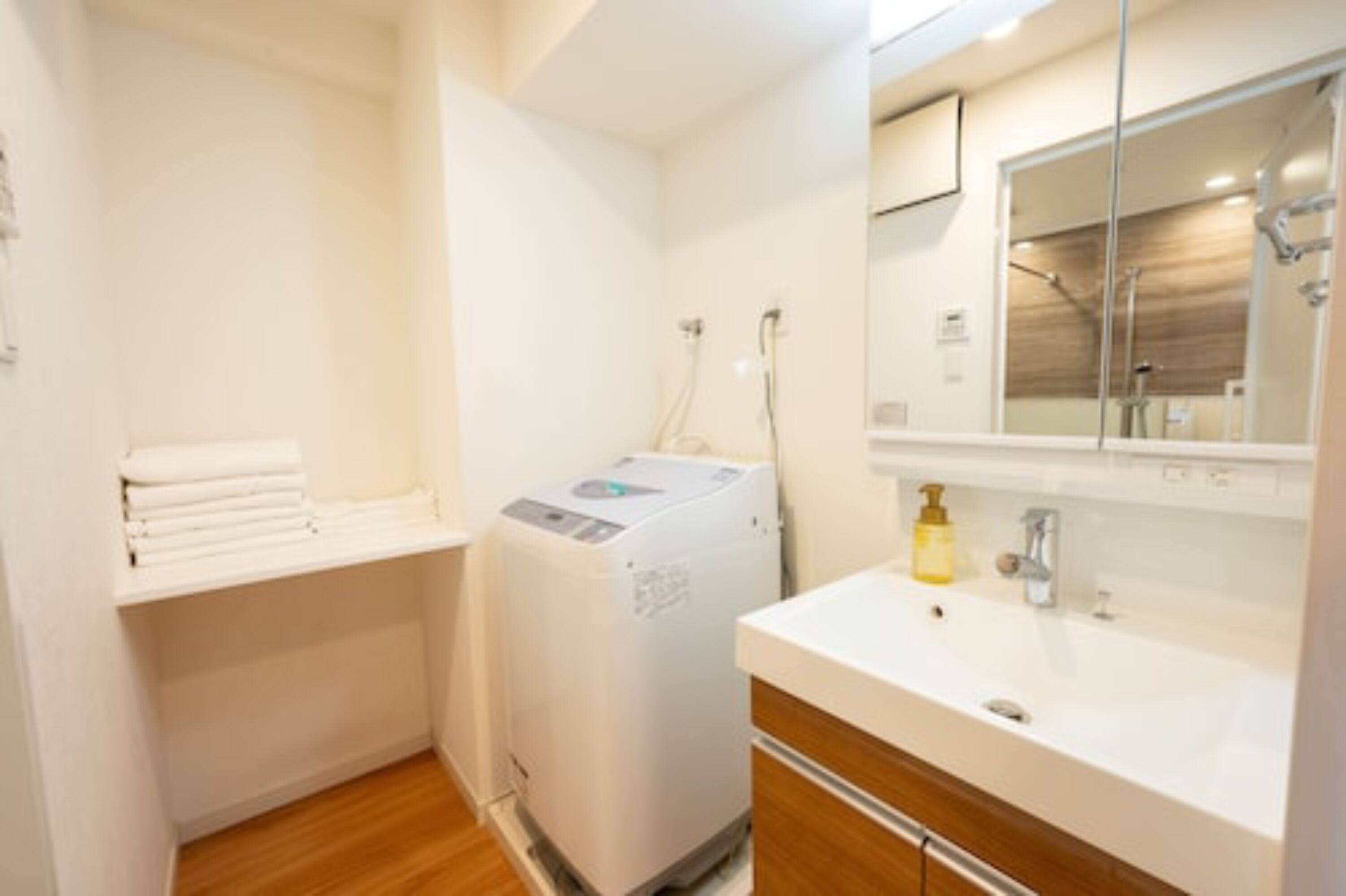 A compact bathroom with a washing machine, a sink, and a mirror.