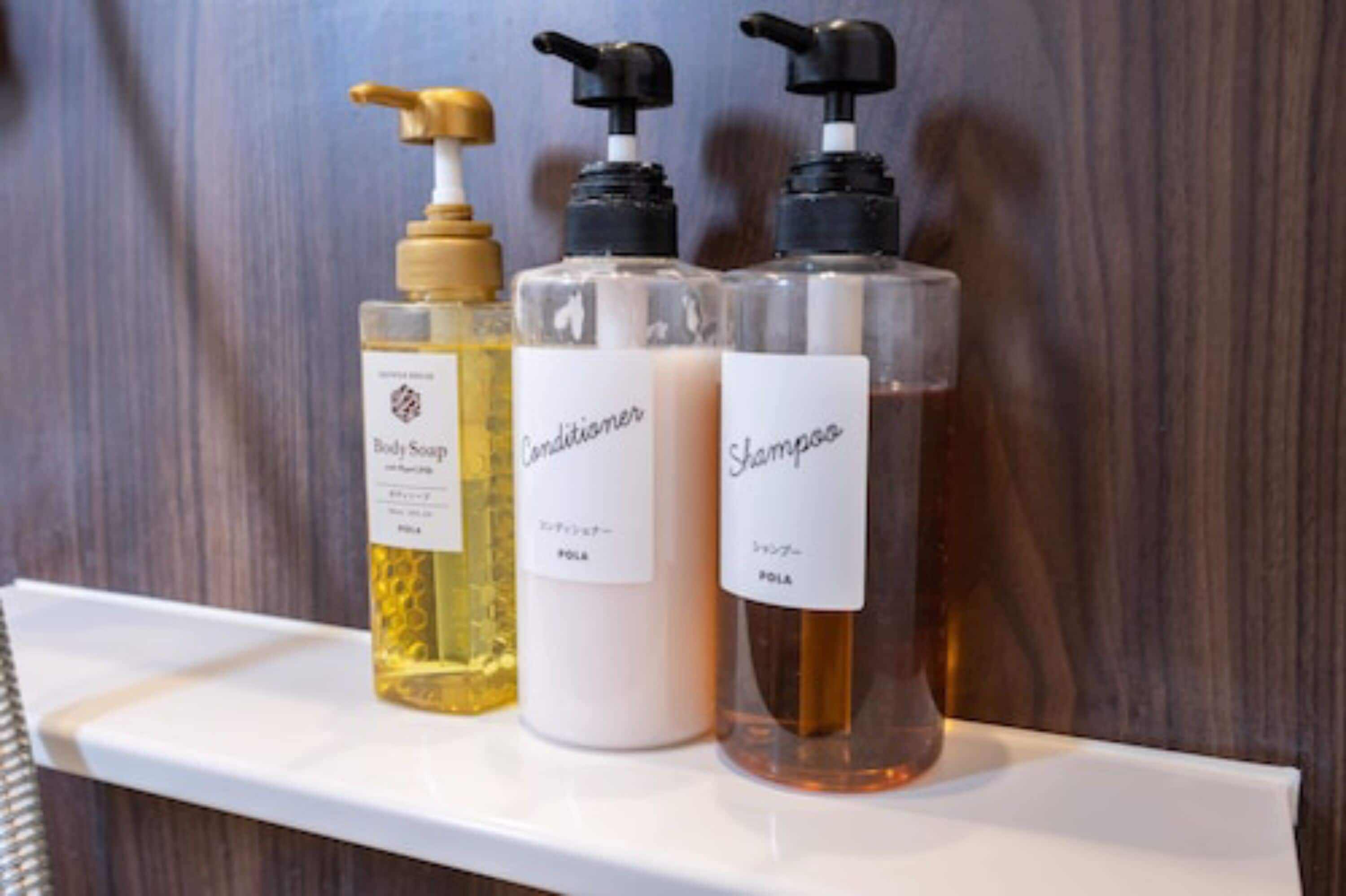 Tres botellas de champú, acondicionador y jabón de baño sobre un estante blanco.