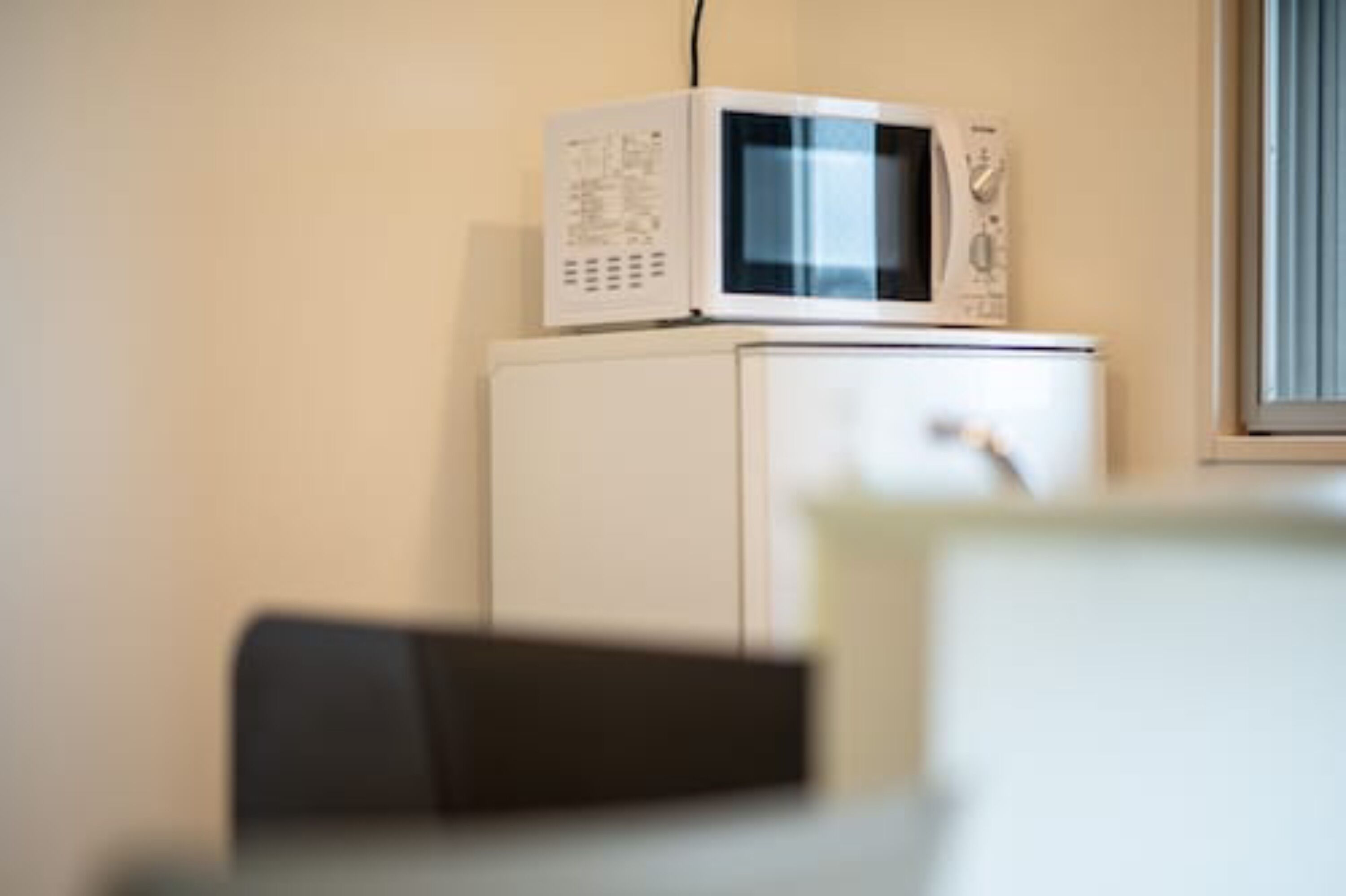 A white microwave on a white cabinet, with a window to the right.