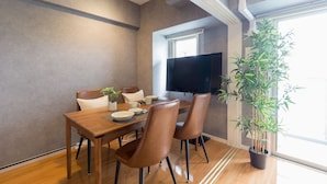 A dining area with a wooden table, four chairs, a potted plant, and a flat-screen TV. - Residence Hotel Hakata 8 (Fukuoka)
