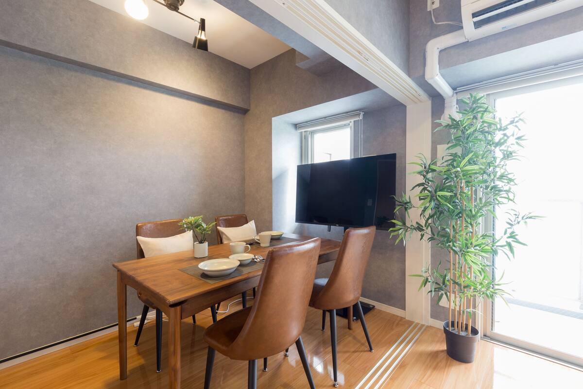 A dining area with a wooden table, four chairs, a potted plant, and a flat-screen TV.