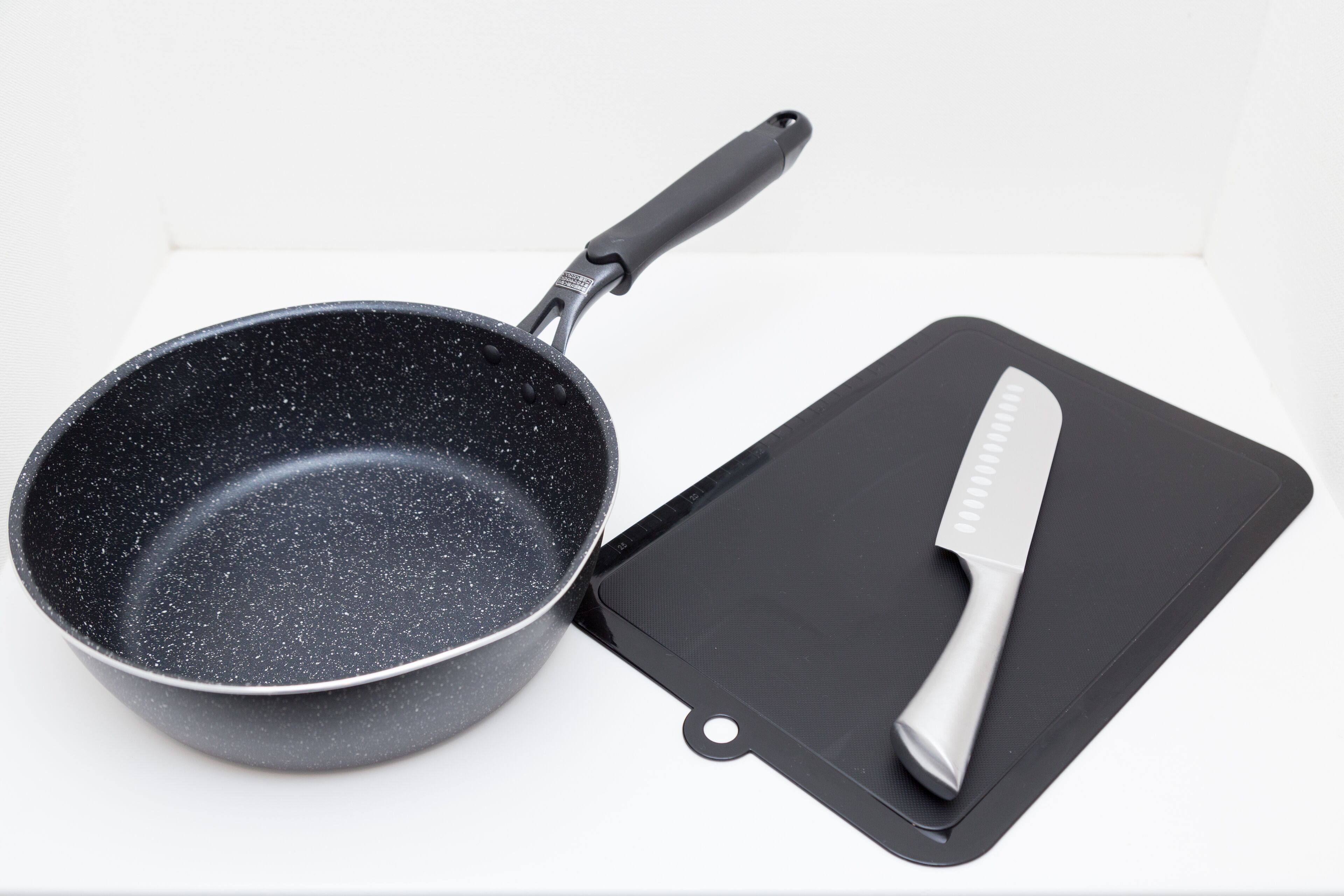 A non-stick frying pan with a black handle and a black cutting board with a knife on it.
