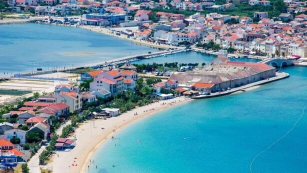 Vue aérienne d’une ville côtière avec une plage, des maisons et un port de plaisance.