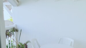 Une terrasse blanche avec une table ronde et quatre chaises, un pot de fleurs et une balustrade blanche.