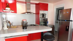 Une cuisine avec des meubles de rangement rouges, un réfrigérateur en acier inoxydable, un four à micro-ondes et une cuisinière à gaz.